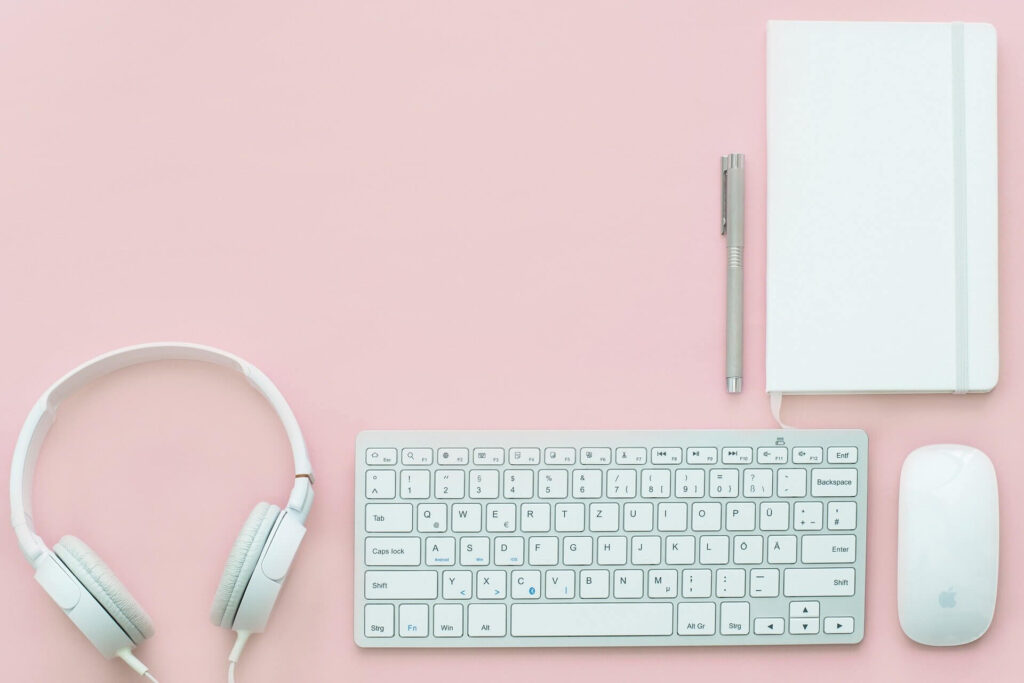 headphones, keyboard, mouse, notepad and pen on a pink surface