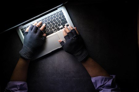 dark room with person typing on a laptop with gloves