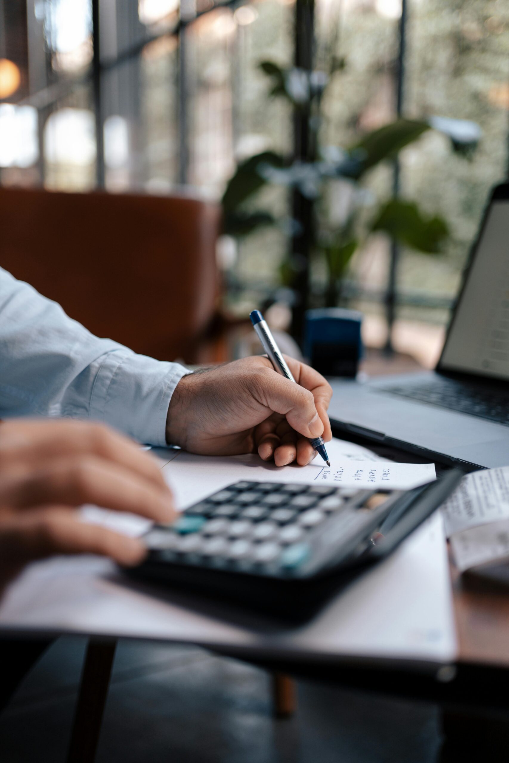 Free A person calculating finances with a calculator and pen on a desk indoors. Stock Photo