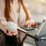 Holding a piggy bank near laptop to represent saving money on security