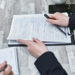 Free Close-up of hands analyzing insurance policy paperwork with pen on table. Stock Photo